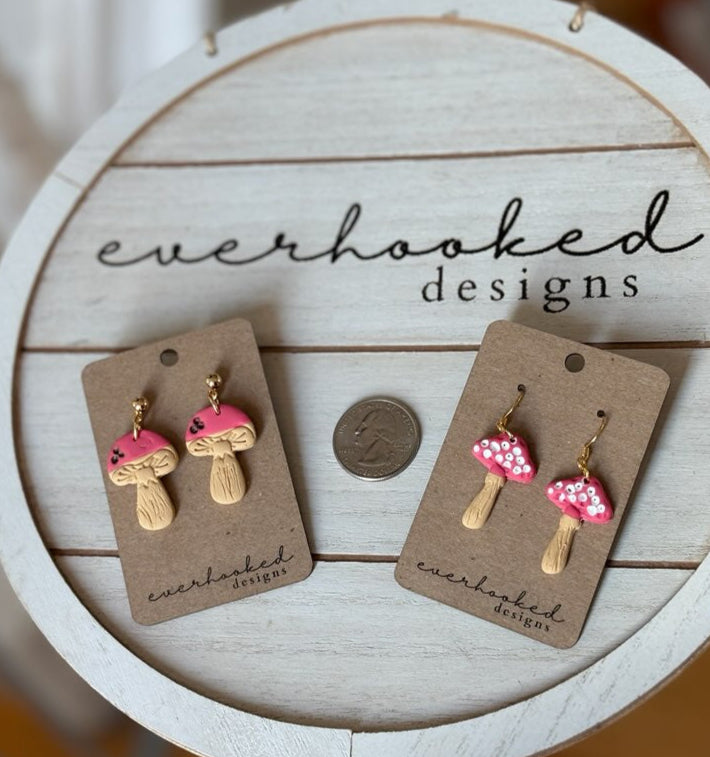 Two pairs of mushroom earrings with pink caps and acrylic painted intricate features. Next to a quarter for comparison