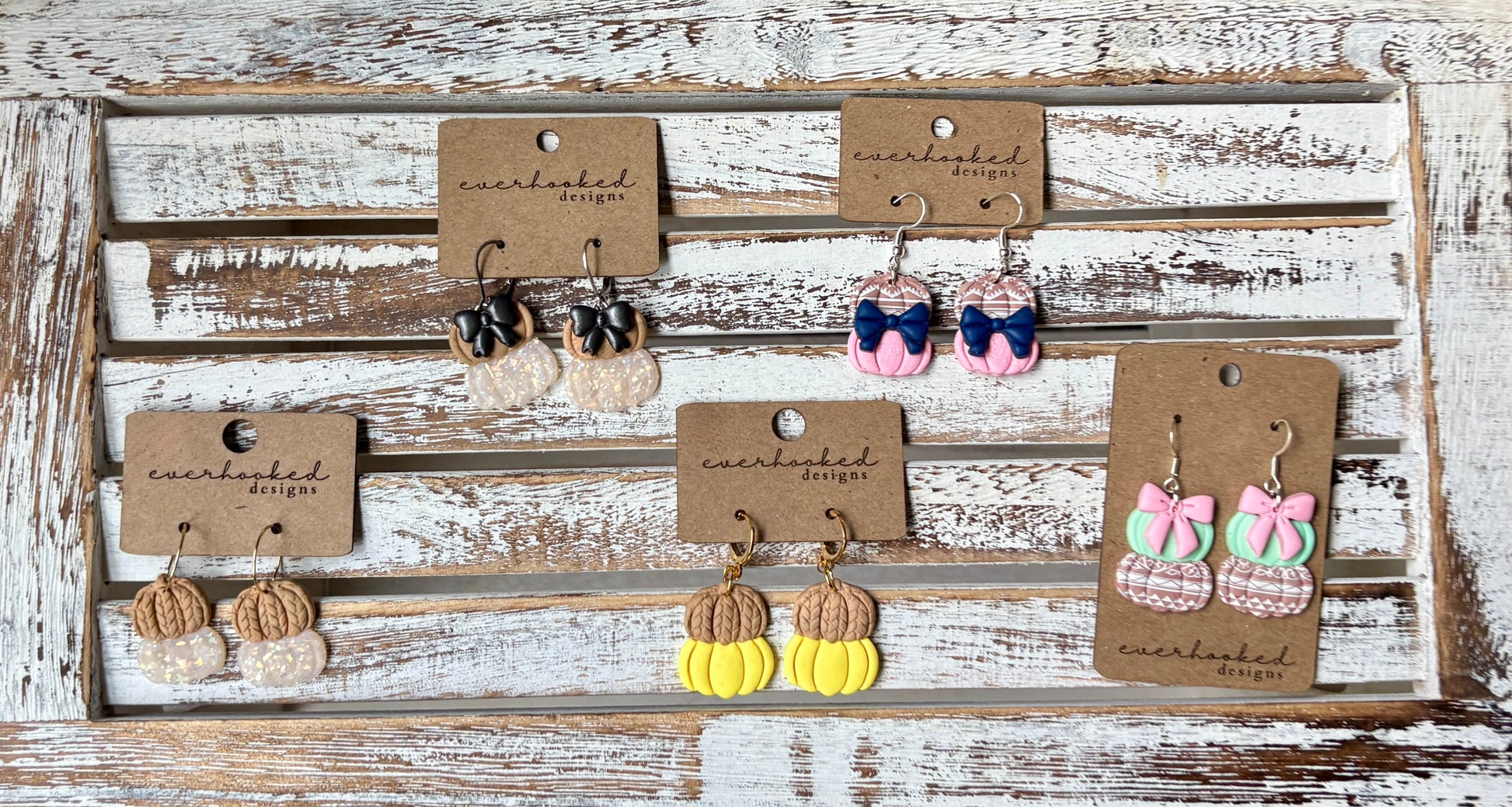 Display of polymer clay double pumpkin dangly earrings (with and without bows) on a rustic wooden board