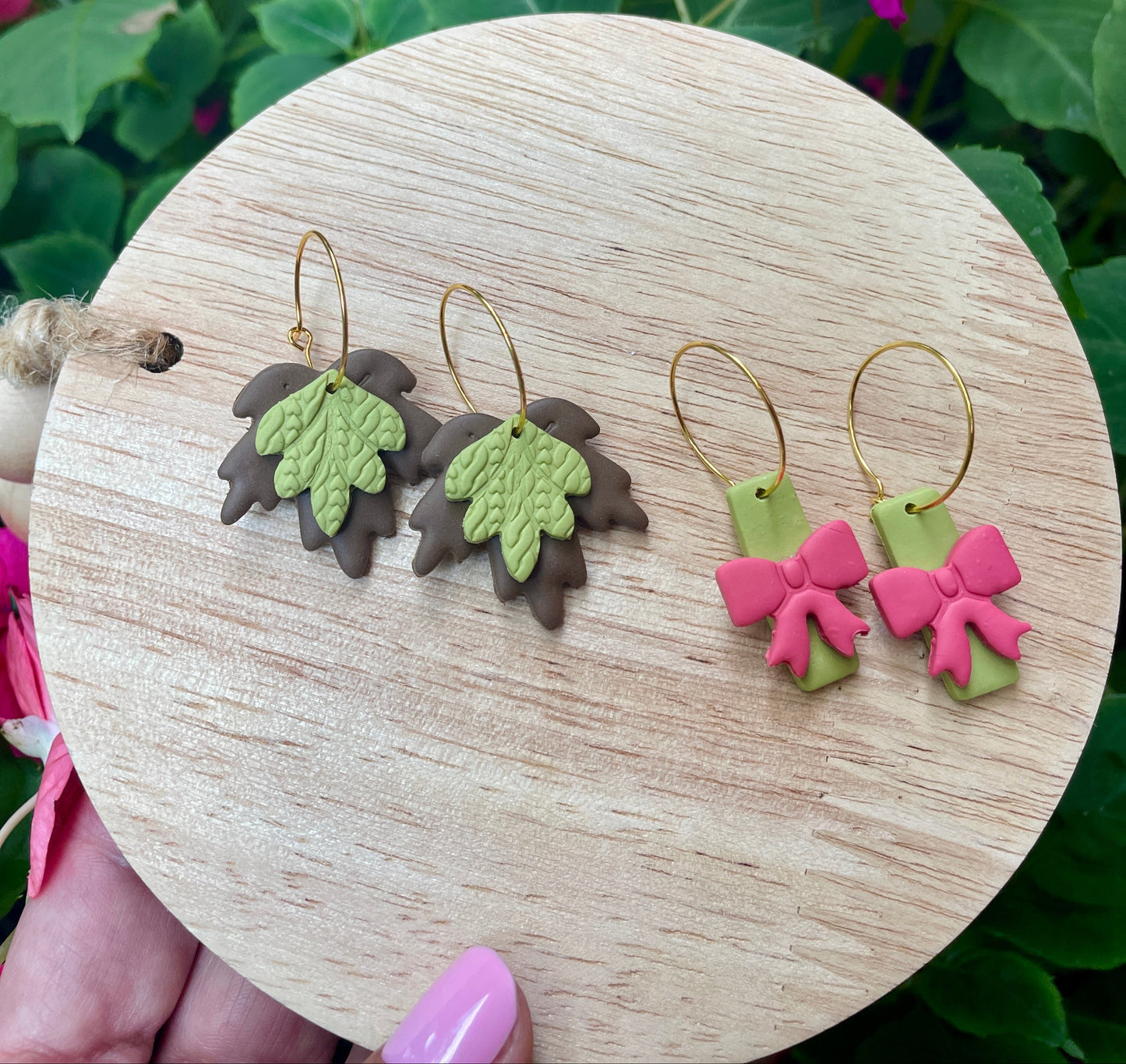 Two pairs of earrings on a wooden round stand with pink flowers in the background