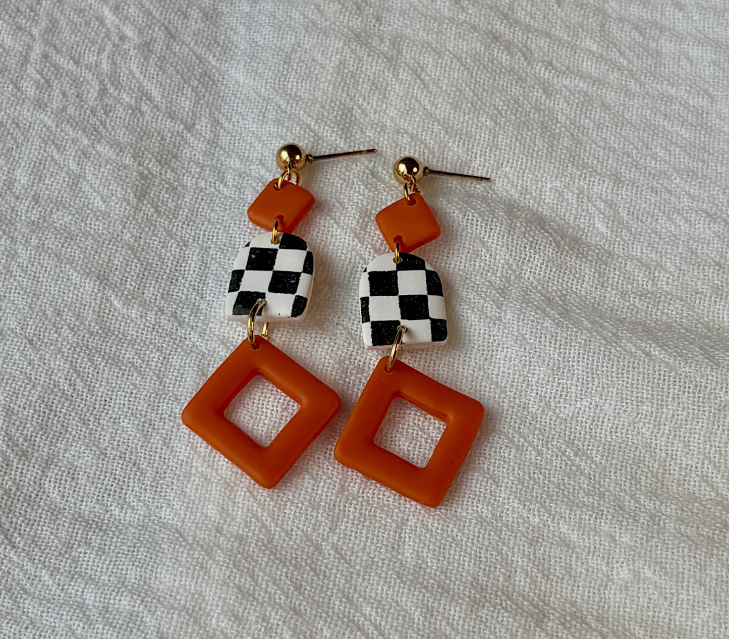 Three piece dangly black and white checkerboard polymer clay earrings with vibrant orange bow accents. Retro-inspired, bold, and playful statement piece