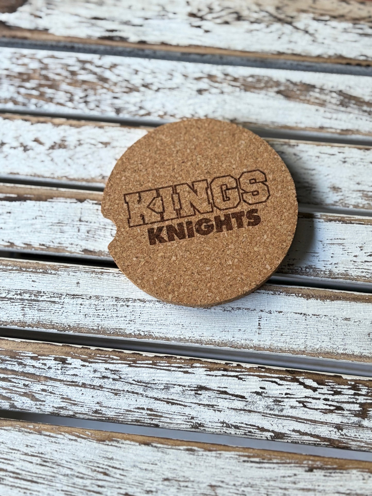 Car cork coaster with 'KINGS KNIGHTS' text on a wooden surface