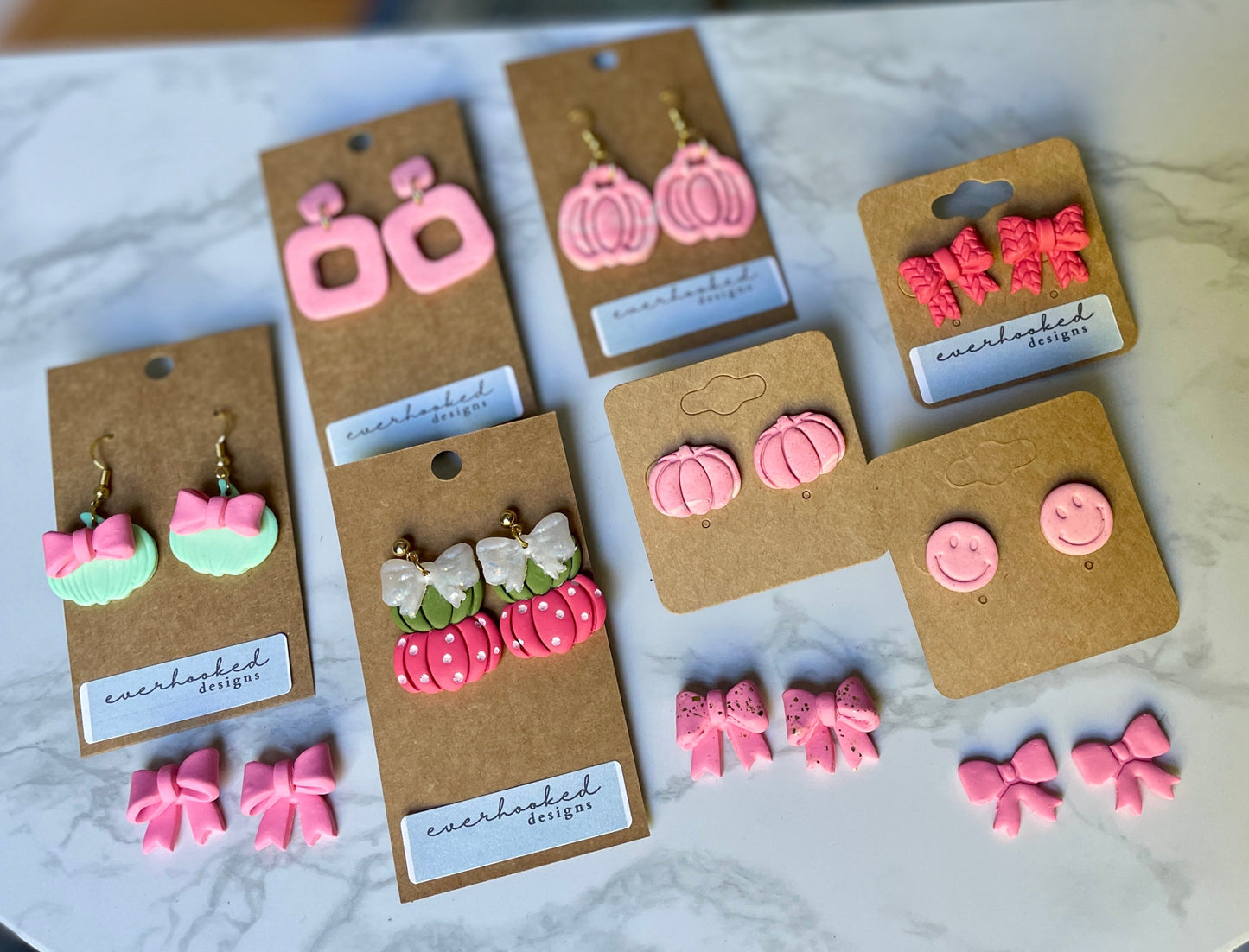 Set of pink earrings on brown card packaging displayed on a marble surface