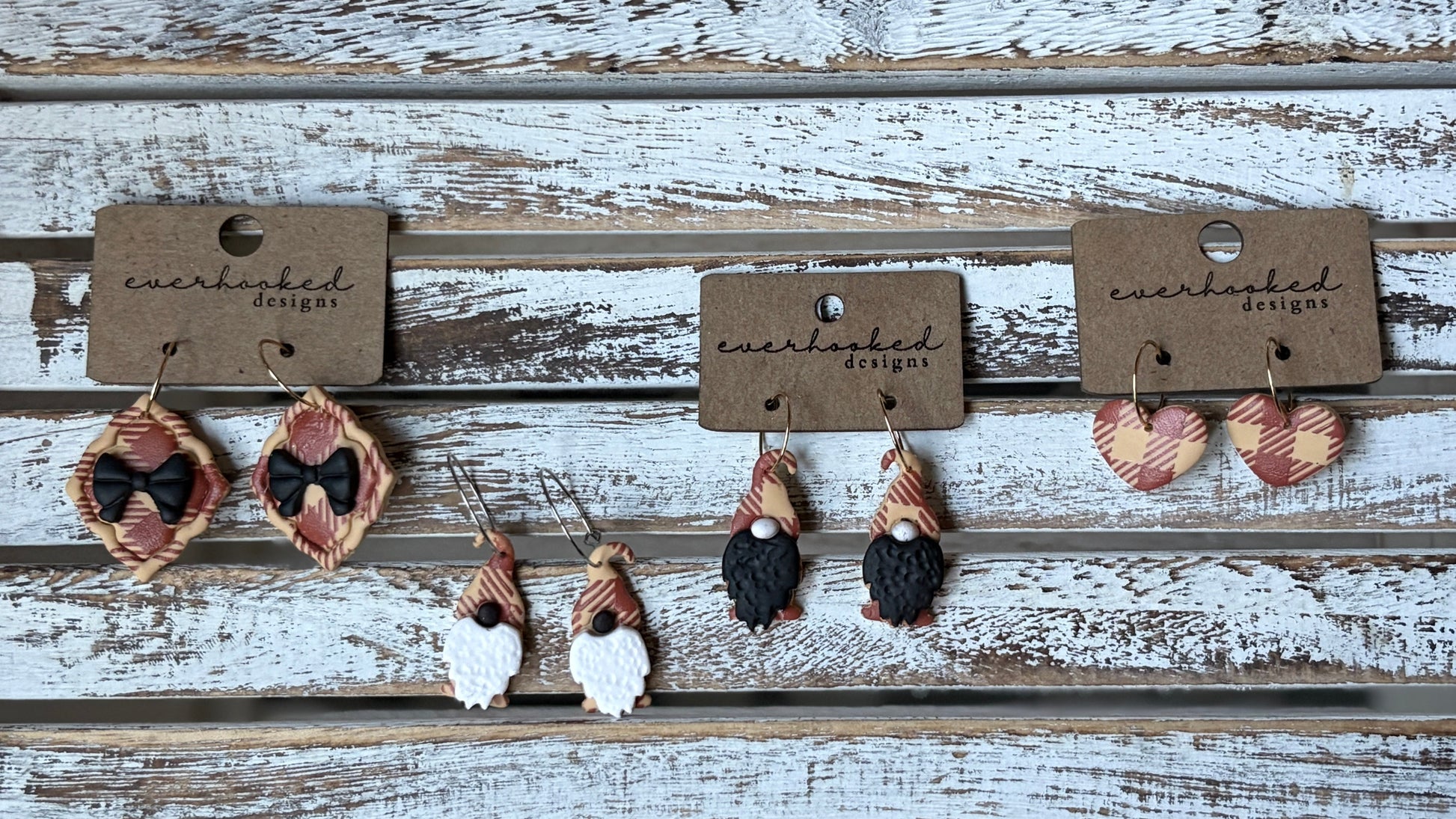 Handmade polymer clay earrings shaped like framed ribbon, whimsical gnomes and hearts on hoops. Each pair has a red and beige plaid design, lightweight and seasonal.