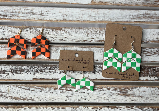 Three pairs of checkerboard clay earrings in a chevron shape, displayed on kraft earring cards. Includes stacked double dangles and mini hoops in orange and black or green and white