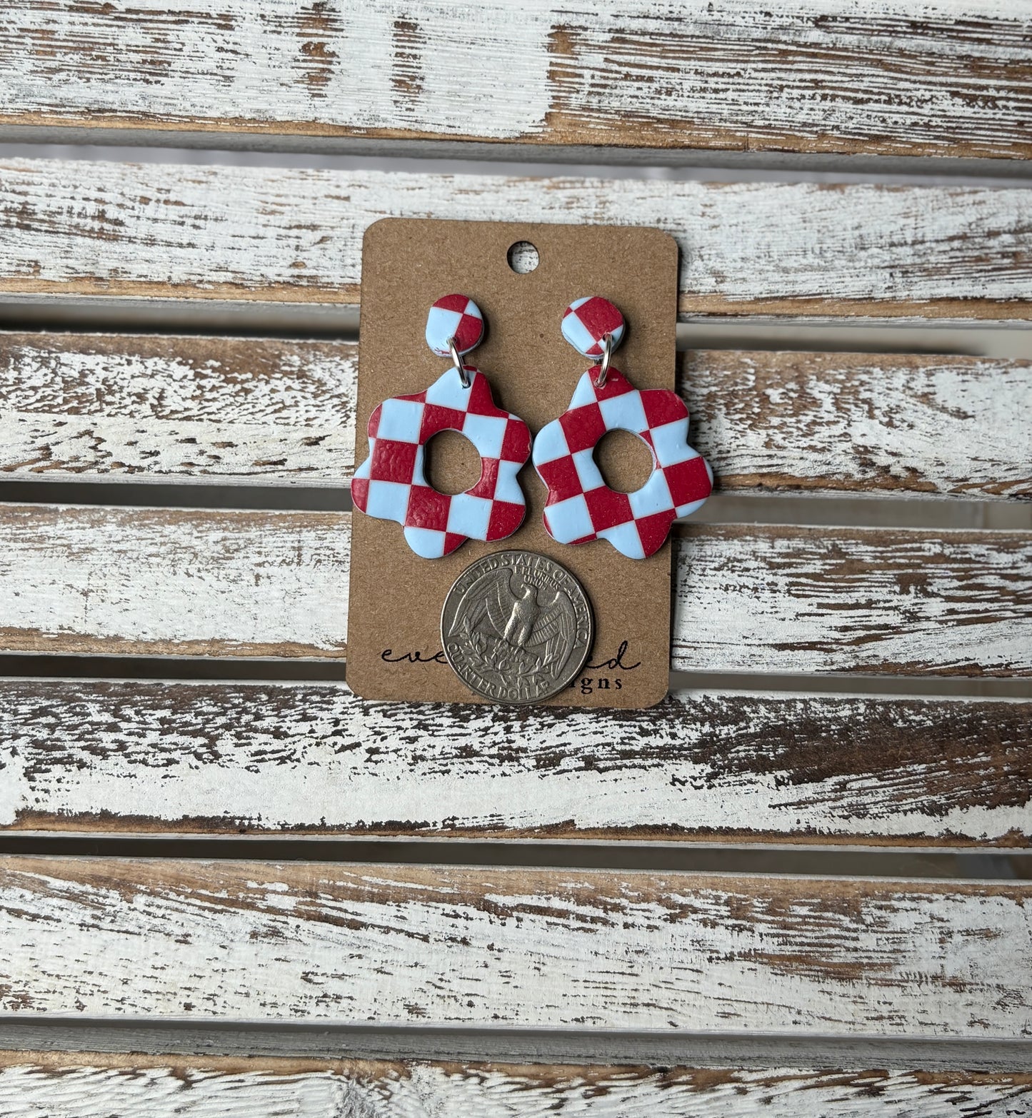 Red and light blue checkerboard clay earrings in a floral cutout shape, displayed on a kraft card with a quarter placed below to show scale.