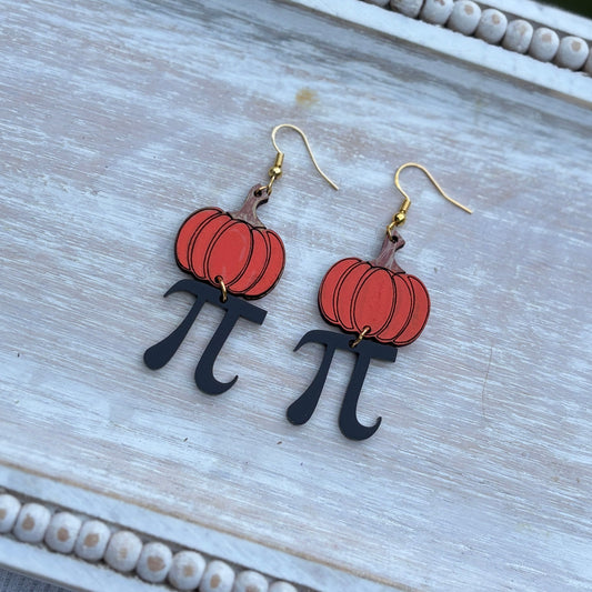 Laser cut pumpkin pi earrings with hand-painted pumpkin tops and black pi symbols, displayed on a wooden tray