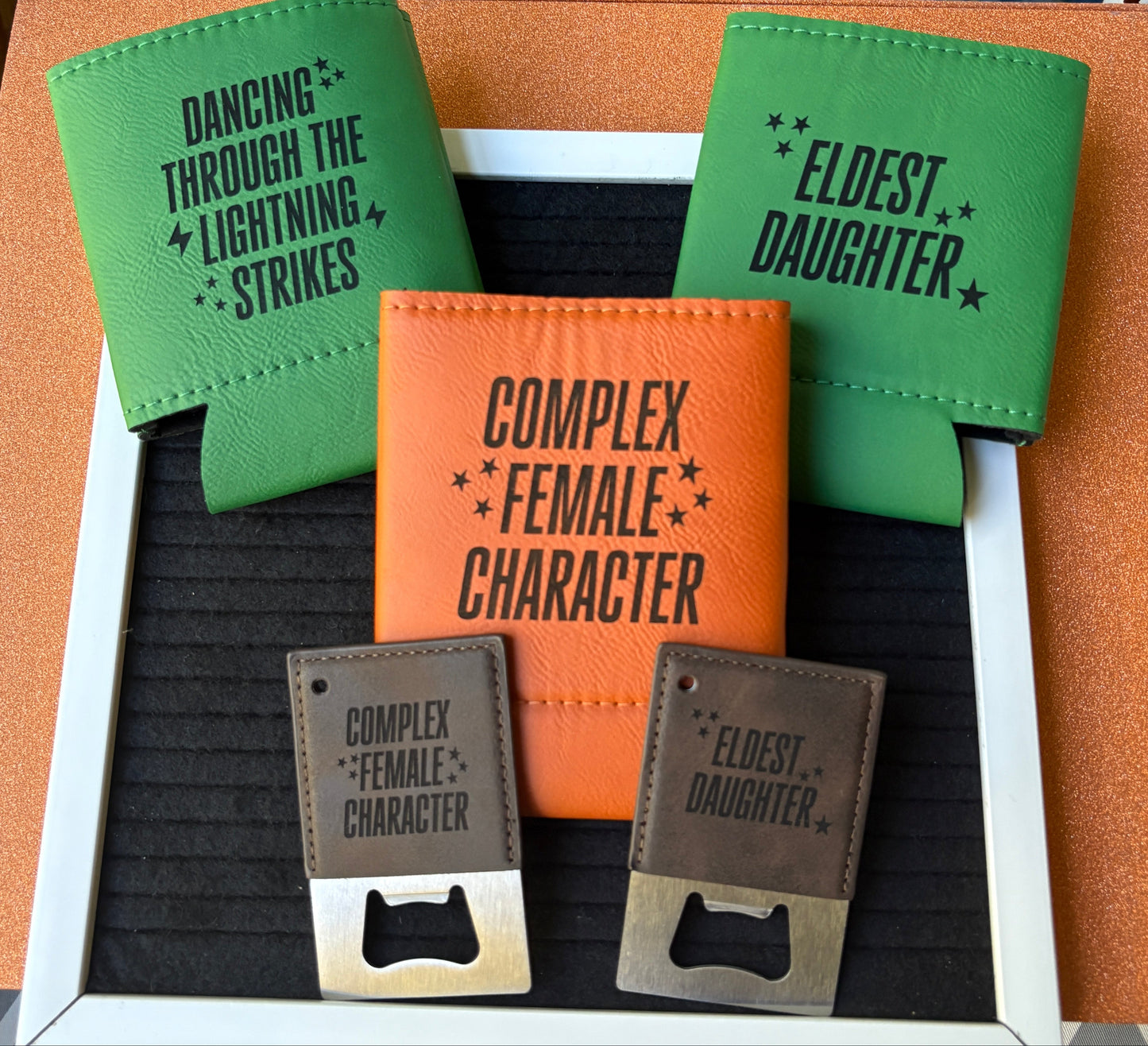 Engraved leatherette koozies and bottle openers with song lyric phrases “Complex Female Character,” “Eldest Daughter,” and “Dancing Through the Lightning Strikes,” handmade lyric-inspired drinkware by Everhooked Designs