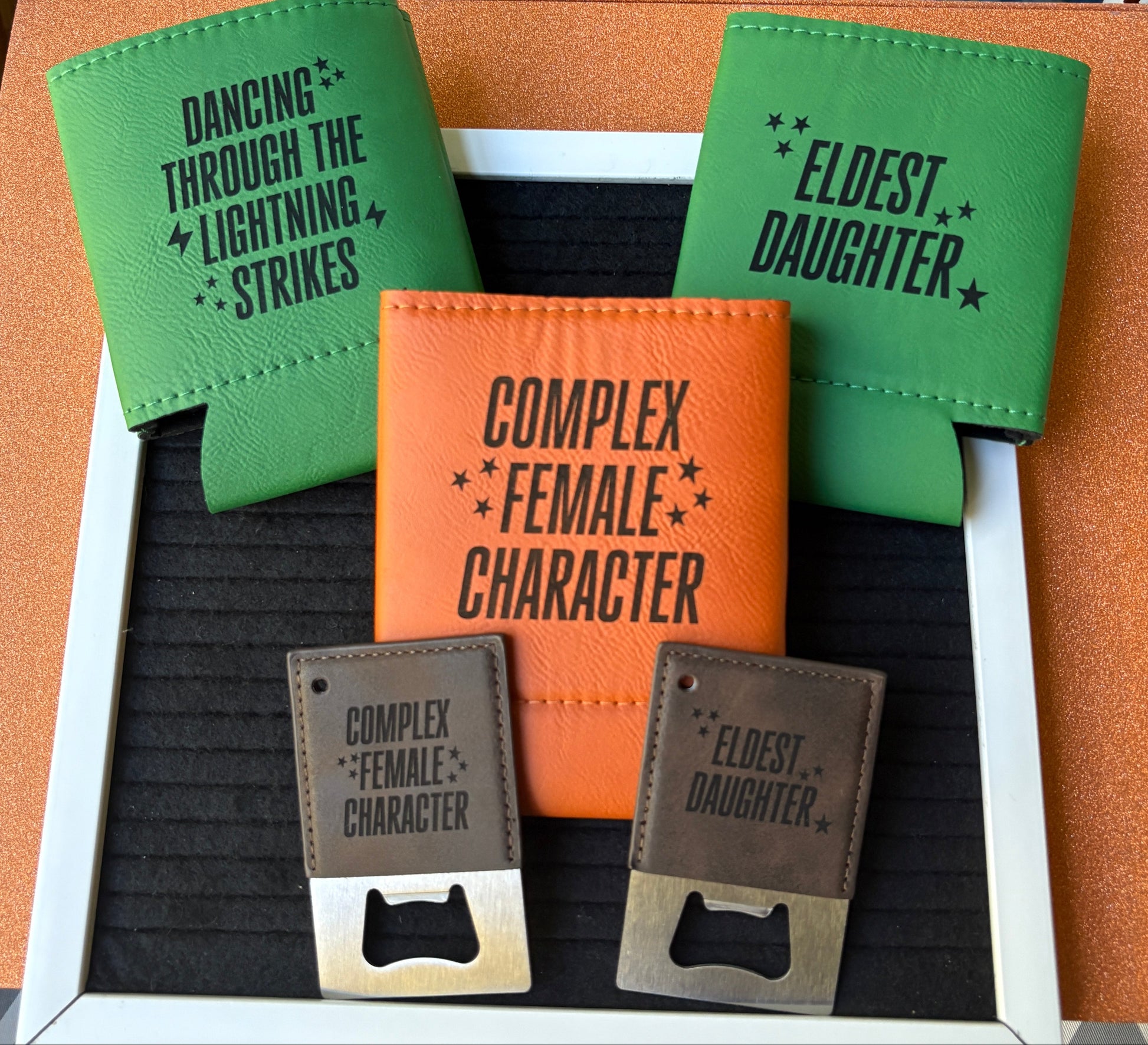 Engraved leatherette koozies and bottle openers with song lyric phrases “Complex Female Character,” “Eldest Daughter,” and “Dancing Through the Lightning Strikes,” handmade lyric-inspired drinkware by Everhooked Designs