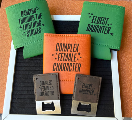 Engraved leatherette koozies and bottle openers with song lyric phrases “Complex Female Character,” “Eldest Daughter,” and “Dancing Through the Lightning Strikes,” handmade lyric-inspired drinkware by Everhooked Designs