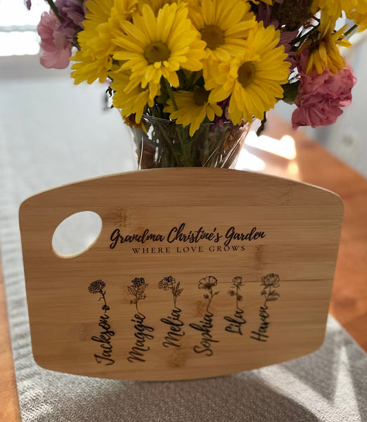 Cutting board with Grandma Christine's Garden on top, then "Where Love Grows," and then below that six names with corresponding birth flowers.