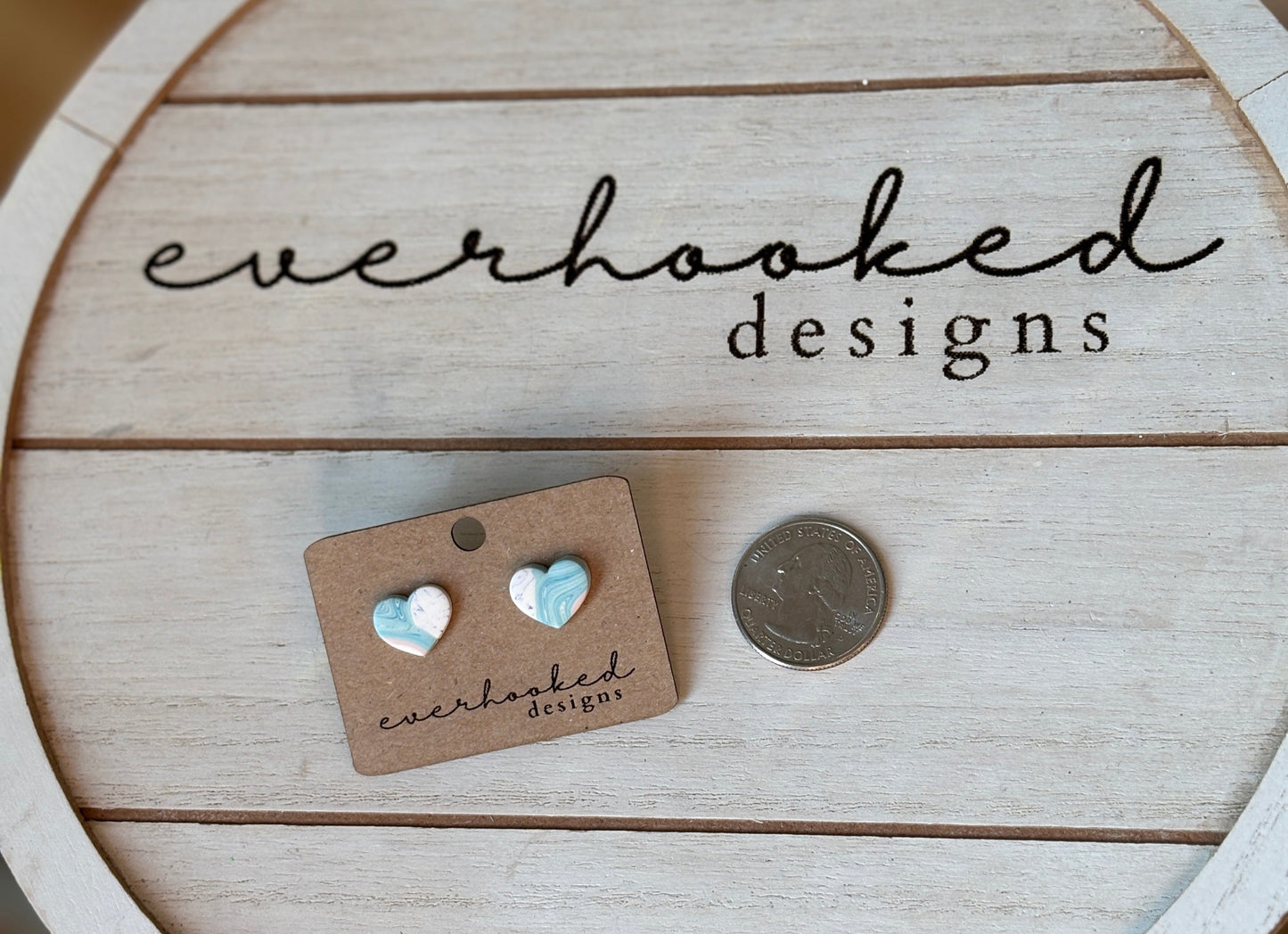 Pastel pink and blue tie dye stud earrings next to quarter for size comparison