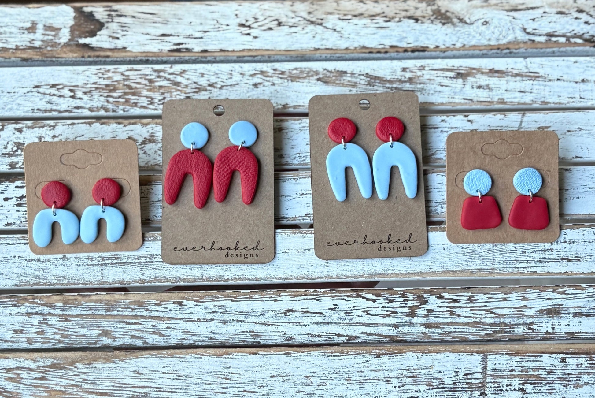 Set of red and light blue earrings on display with branded cards on a wooden surface