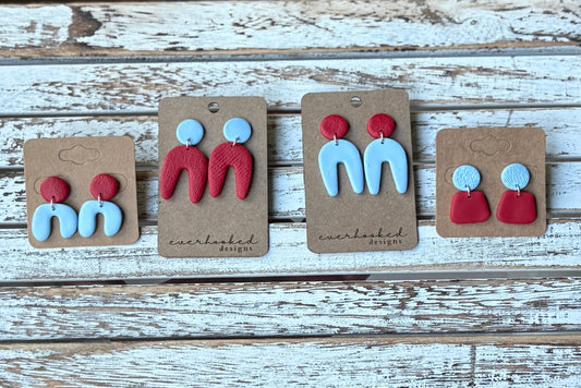 Set of red and light blue earrings on display with branded cards on a wooden surface