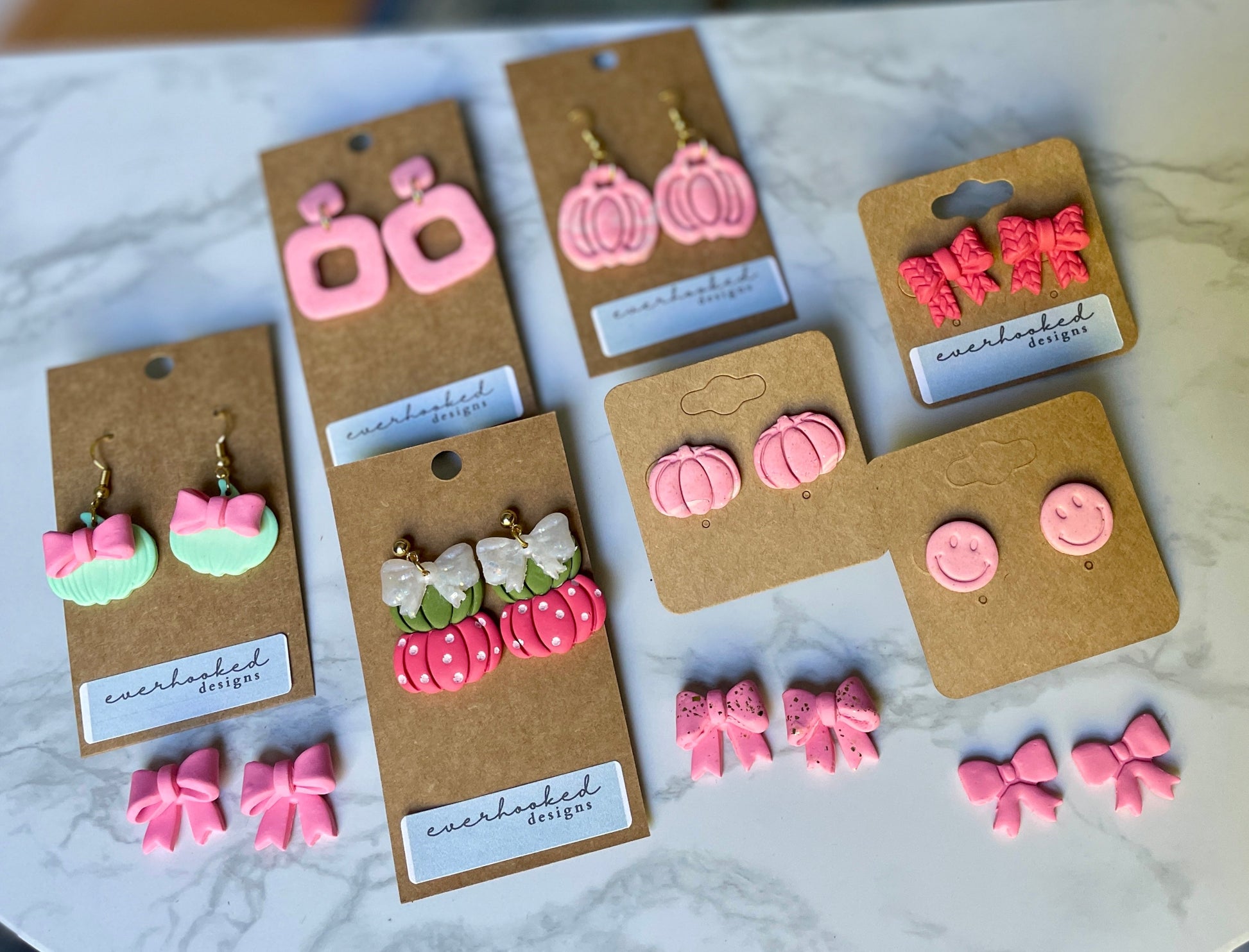 Set of pink earrings on brown card packaging displayed on a marble surface