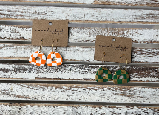 Two pairs of mini checkerboard clay earrings with gold hoops, displayed on kraft cards in orange and white, and green and gold color combos