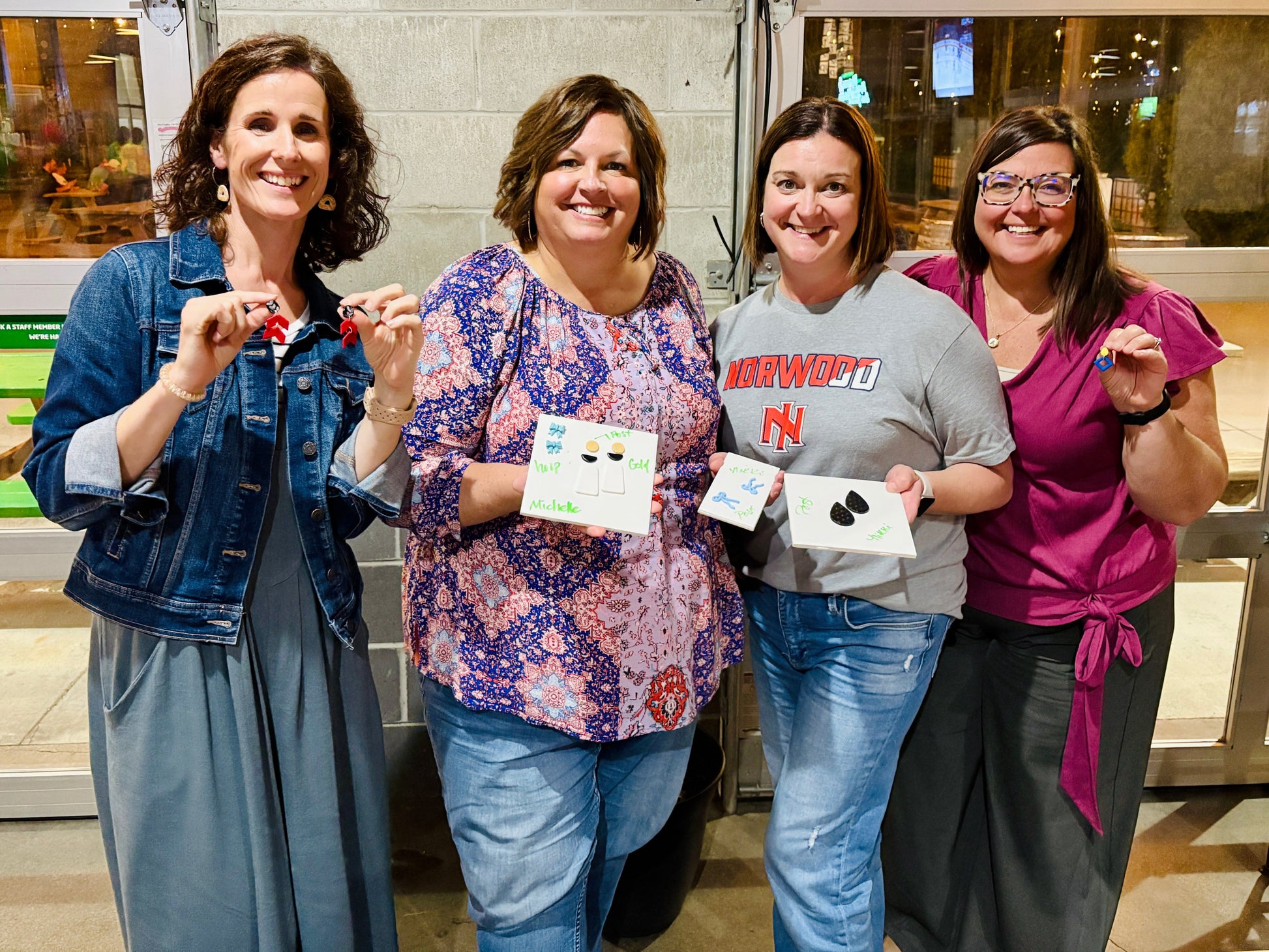 Four women smiling and holding up their finished clay earrings at the end of a Sonder workshop.